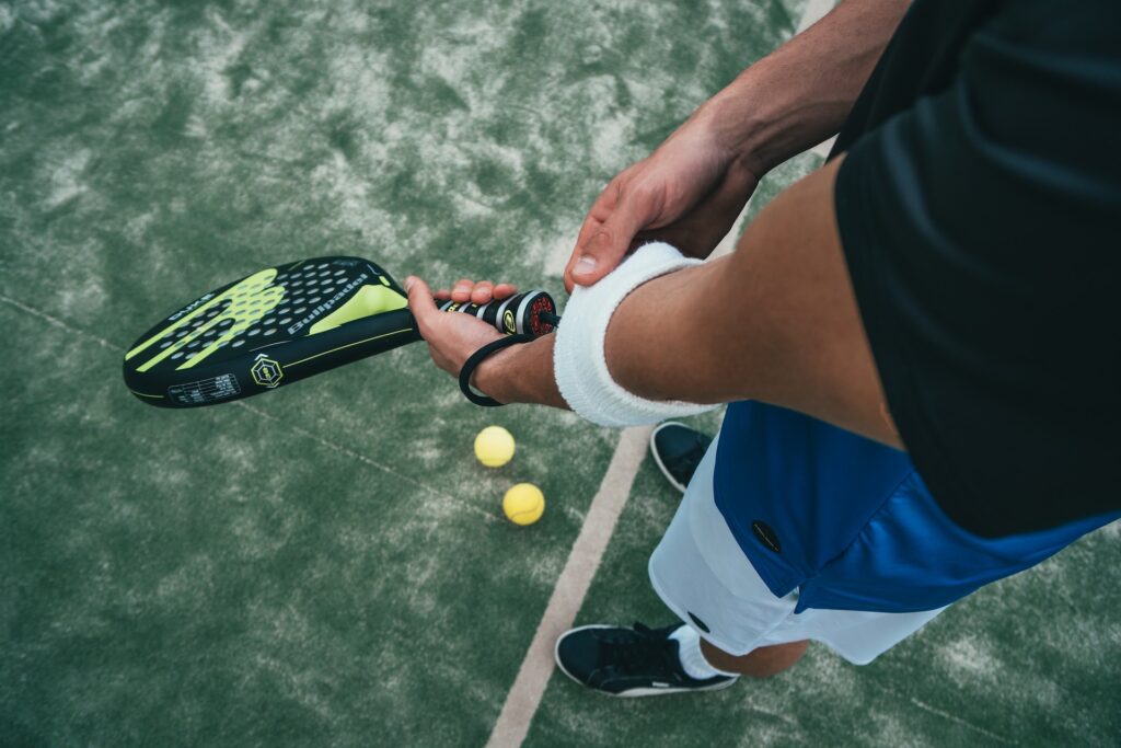 Un hombre con una raqueta de tenis en la mano, una muñequera en la muñeca y pelotas de tenis delante de él.